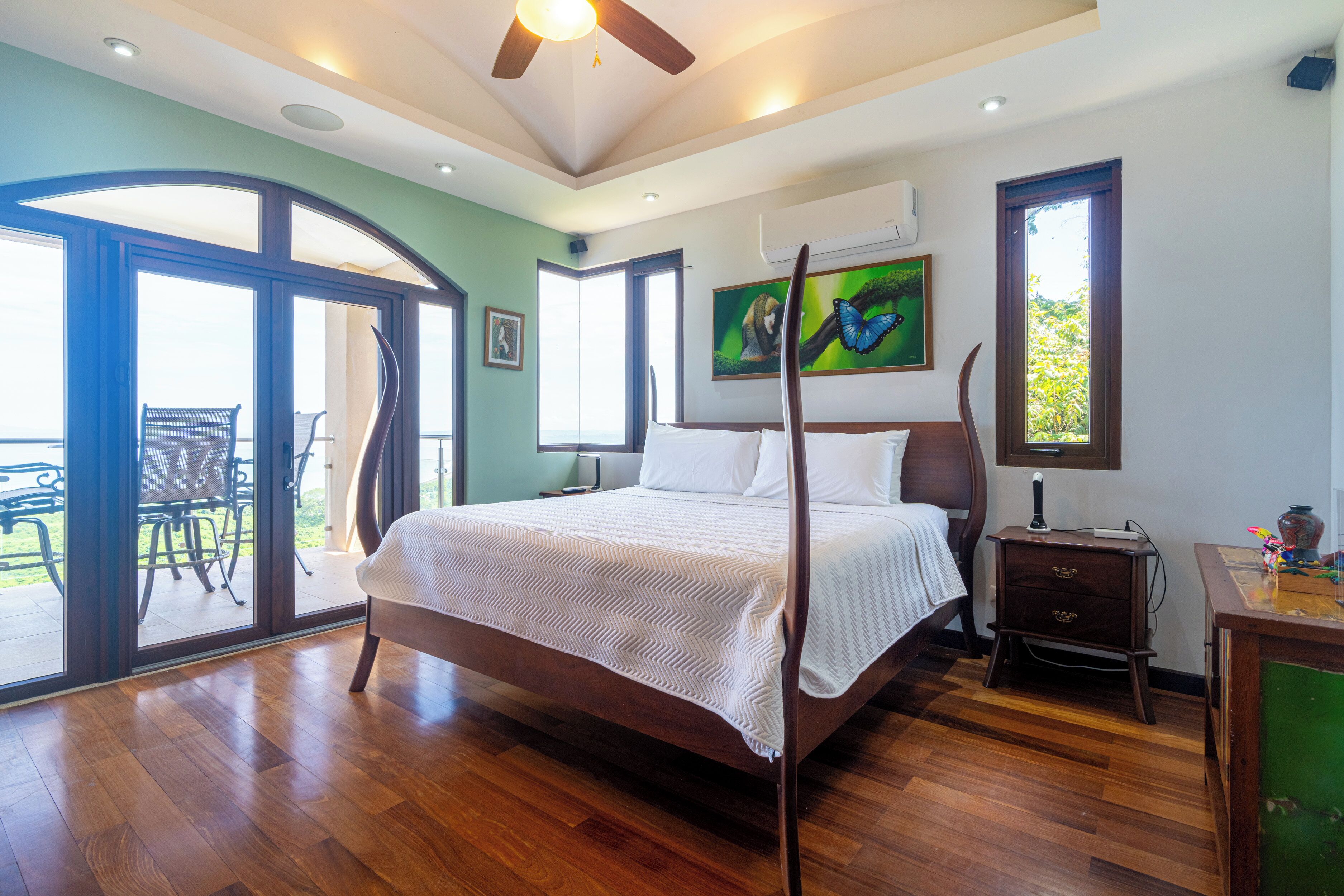 Un dormitorio amplio con una cama grande, ventilador de techo y vistas al exterior por un ventanal.