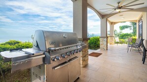 Patio esterno con griglia a gas Weber, colonne in pietra e ventola a soffitto.