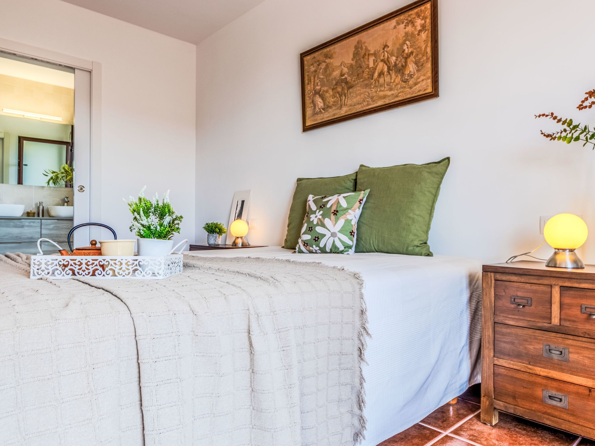 A bedroom with a bed, bedside table, lamp, and a painting on the wall.