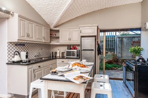 Enjoy cooking and dining in this kitchen with a sink, stove, microwave, refrigerator, and kettle, opening up to a small outdoor area with a potted plant.