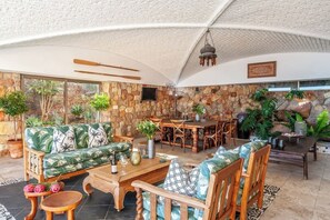 Amplio espacio interior con pared de piedra, muebles de madera y plantas en macetas.
