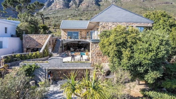 A stone house with a pool, outdoor seating, and a view of rocky mountains.