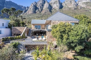 Una casa de piedra con piscina, mobiliario exterior y vistas a montañas rocosas.