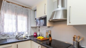 A modern kitchen with a built-in microwave, a stainless steel range hood, and a black induction cooktop. There is a sink with a faucet, a cutting board with lemons, and a knife block.