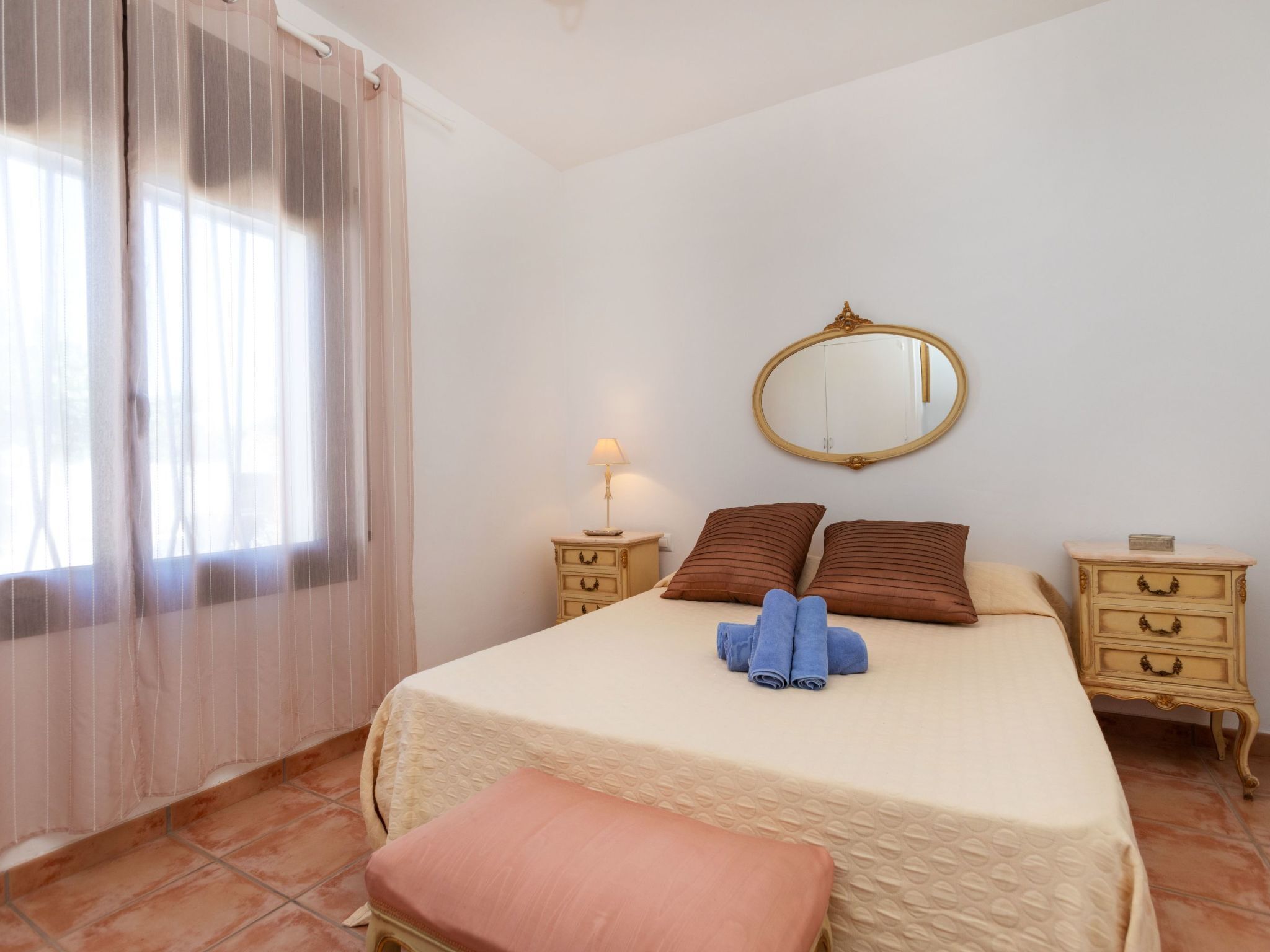 Une chambre à coucher avec un lit, une table de chevet avec une lampe, un miroir et une fenêtre avec des rideaux.