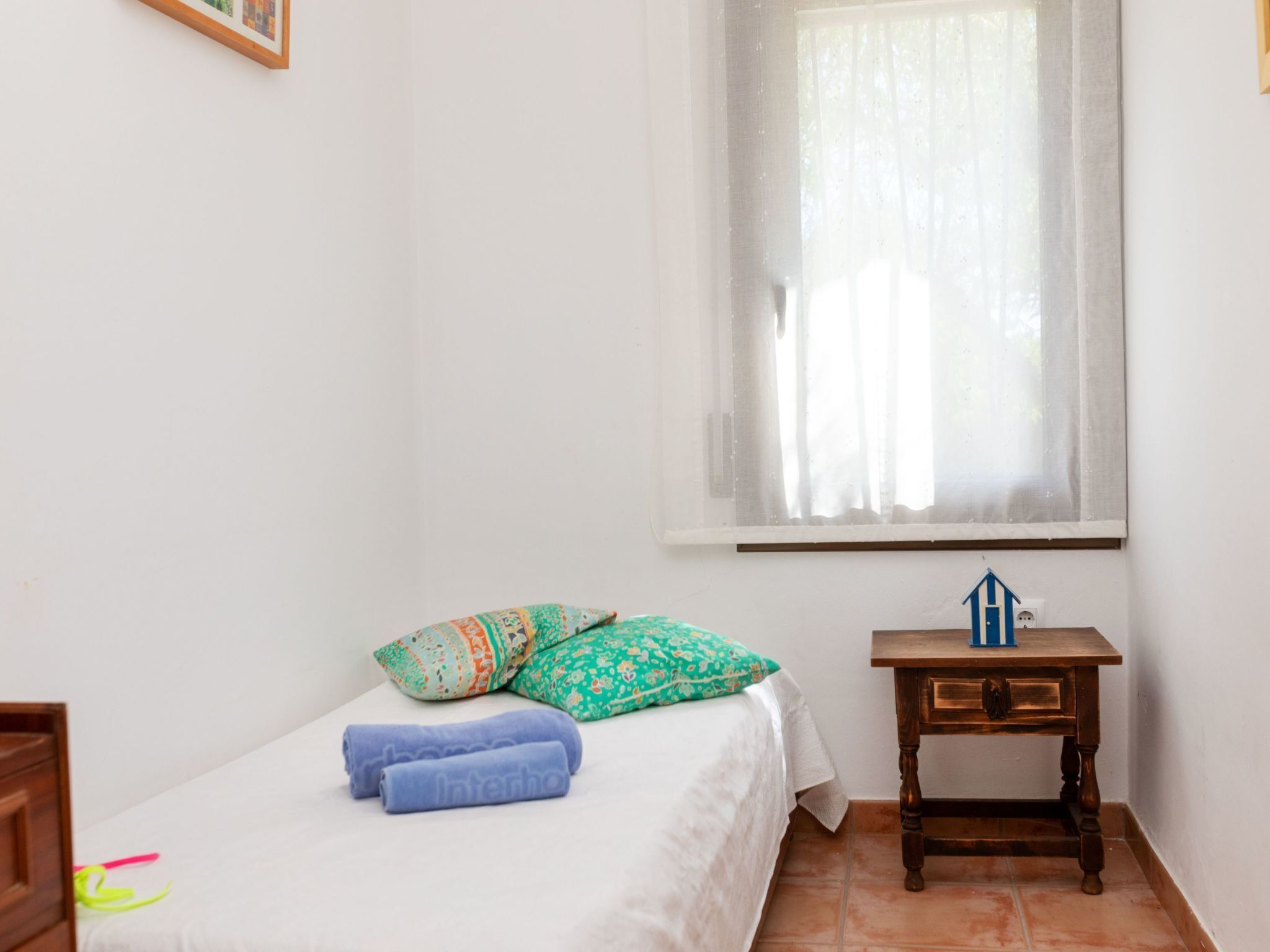 A small, tidy room with a single bed, a nightstand, and a window with sheer curtains.