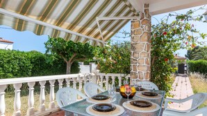 An outdoor dining area with a table set for four, surrounded by white chairs, under a striped awning.