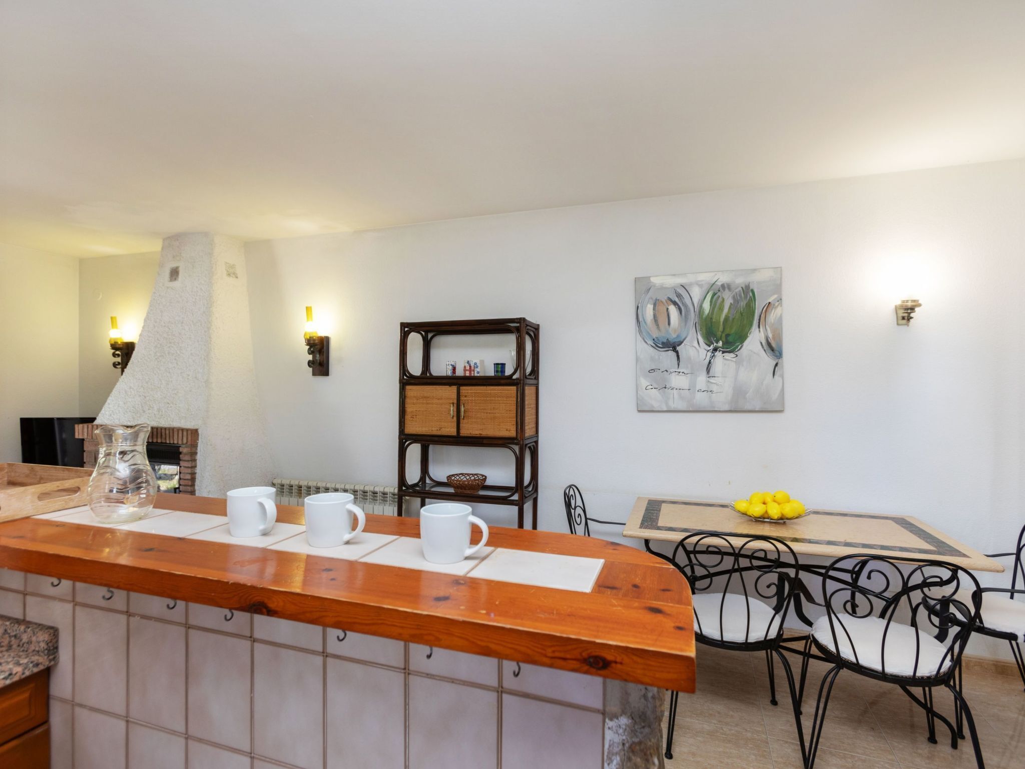 Un coin repas avec un comptoir en bois, des tasses blanches, un panier en osier et une table ornée de citrons jaunes.