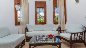 Une pièce confortable avec un canapé, deux fauteuils, une table basse en verre et une fenêtre avec des rideaux.