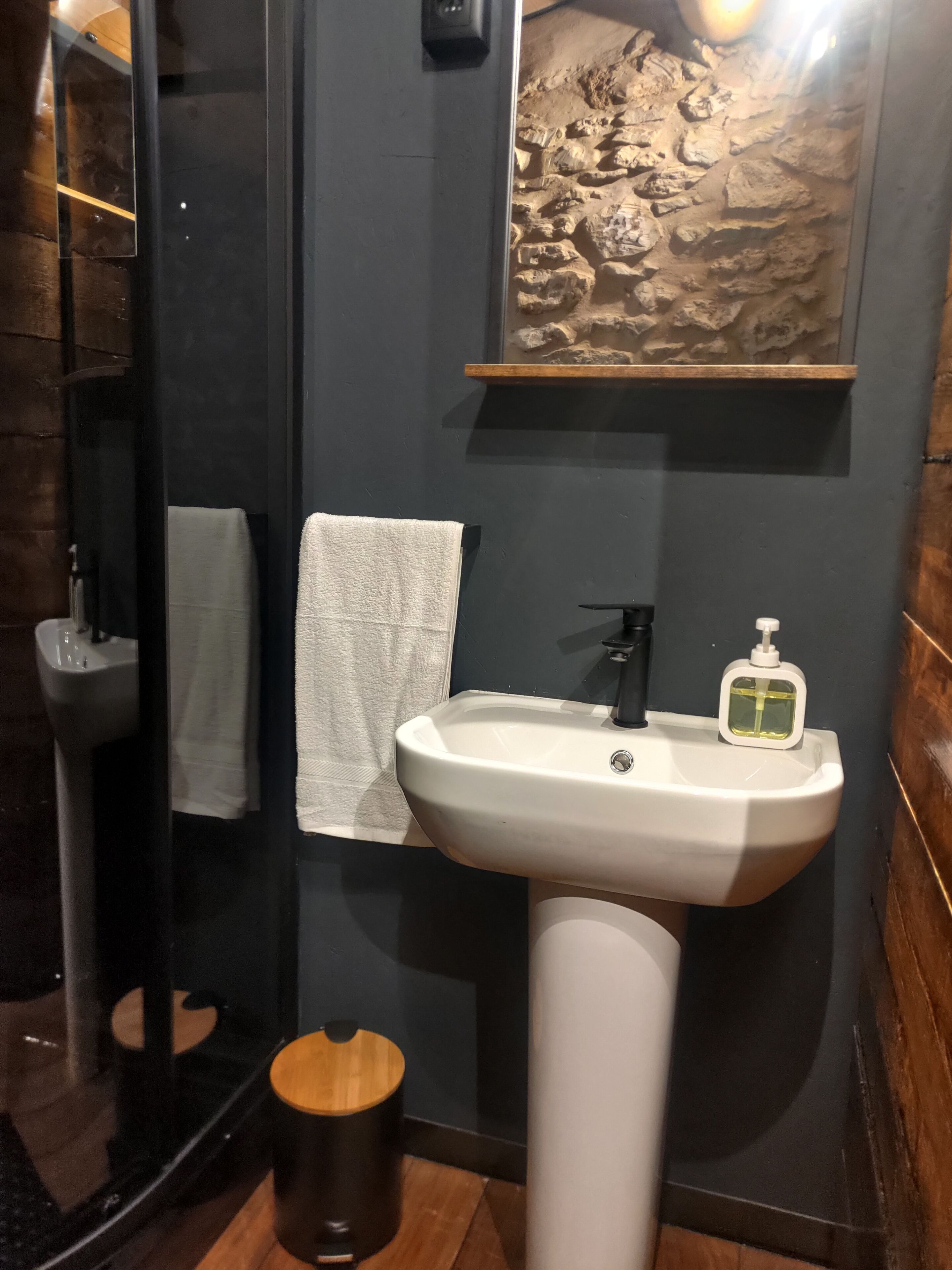 A modern bathroom with a white sink, a mirror, a towel, and a wooden stool.