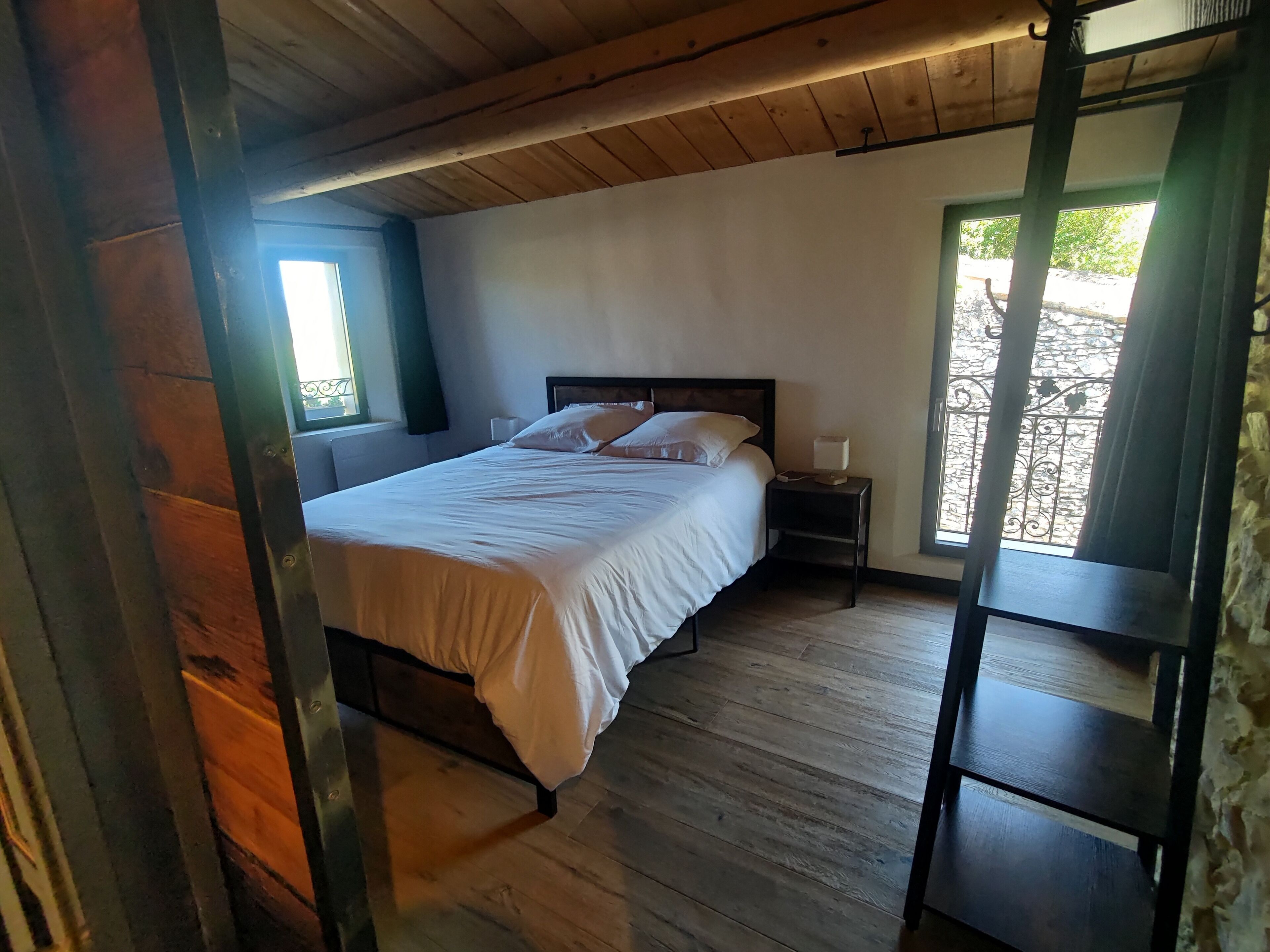 A bedroom with a wooden bed, a nightstand, a window, and a view of the outside.