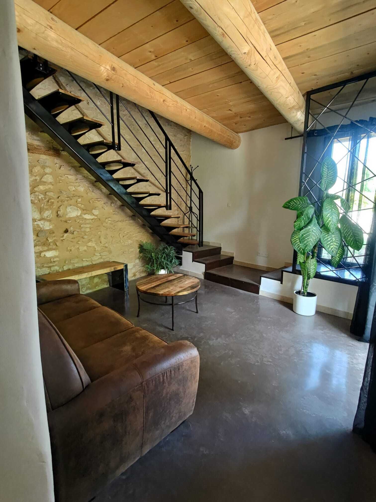 A modern living room with a stone wall, a wooden staircase, a leather sofa, a round wooden coffee table, and two potted plants.