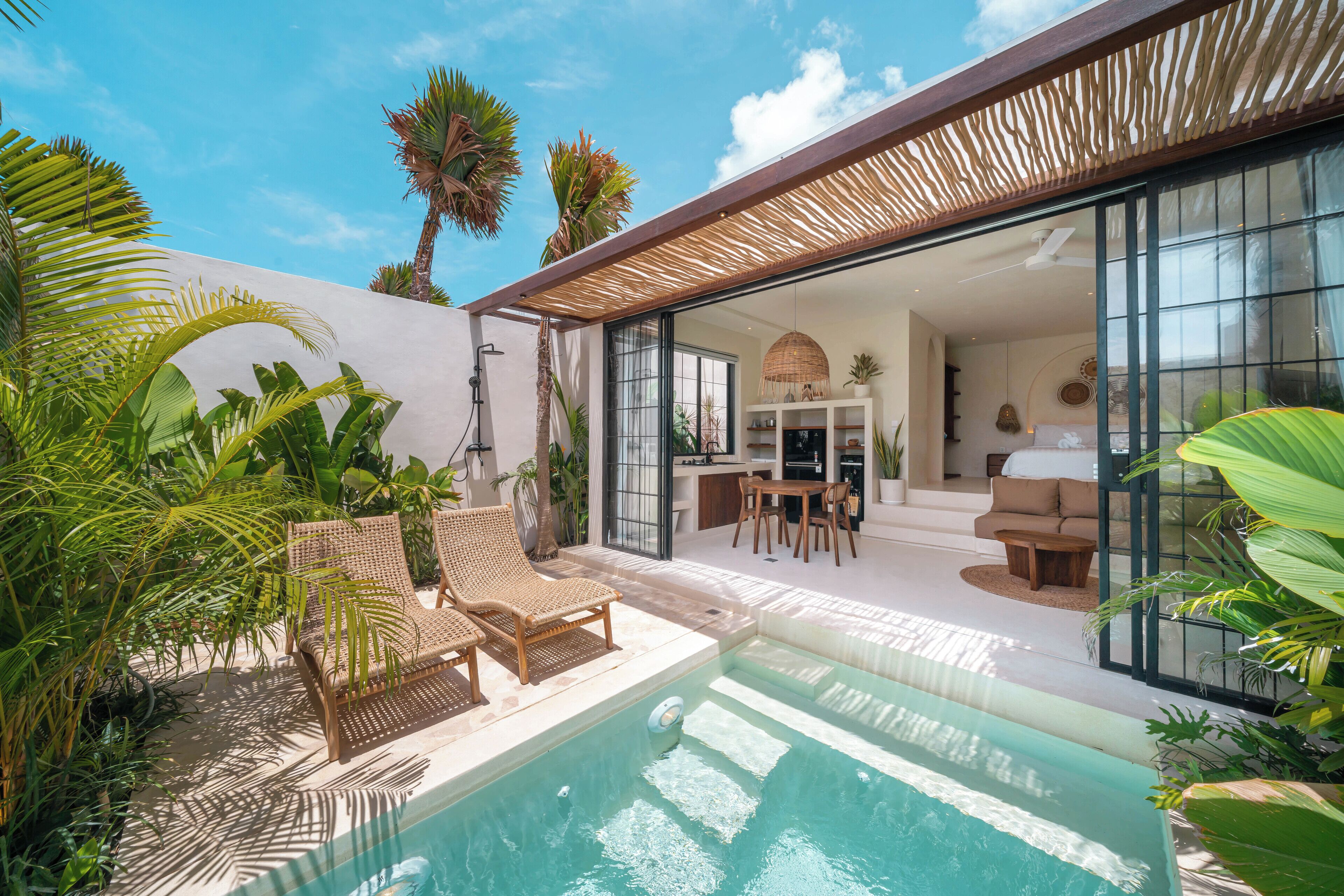 A modern outdoor pool area with lounge chairs, a dining area, and a large sliding glass door leading to a living space.
