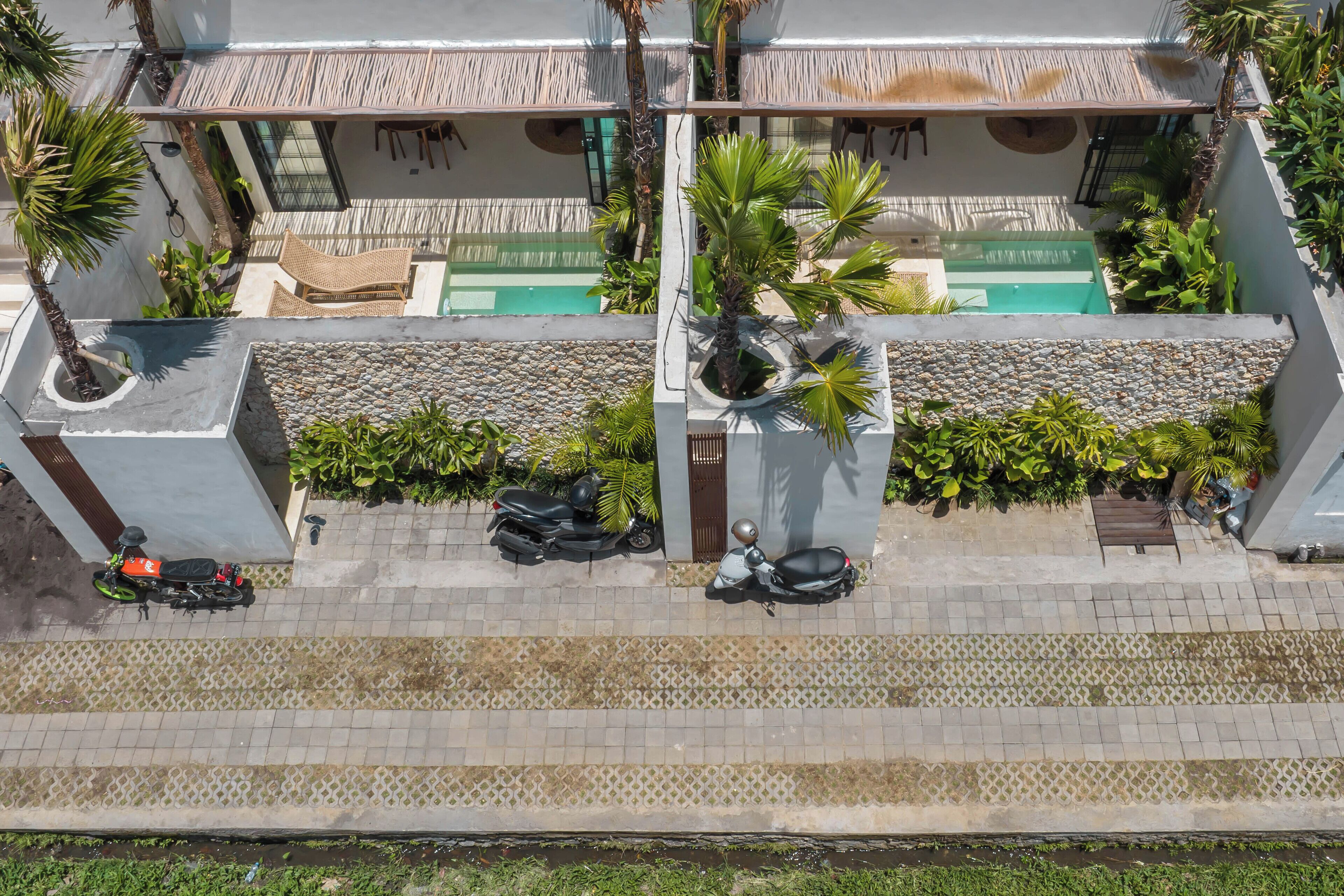 An aerial view of a hotel with a pool, palm trees, and a staircase leading to the entrance.