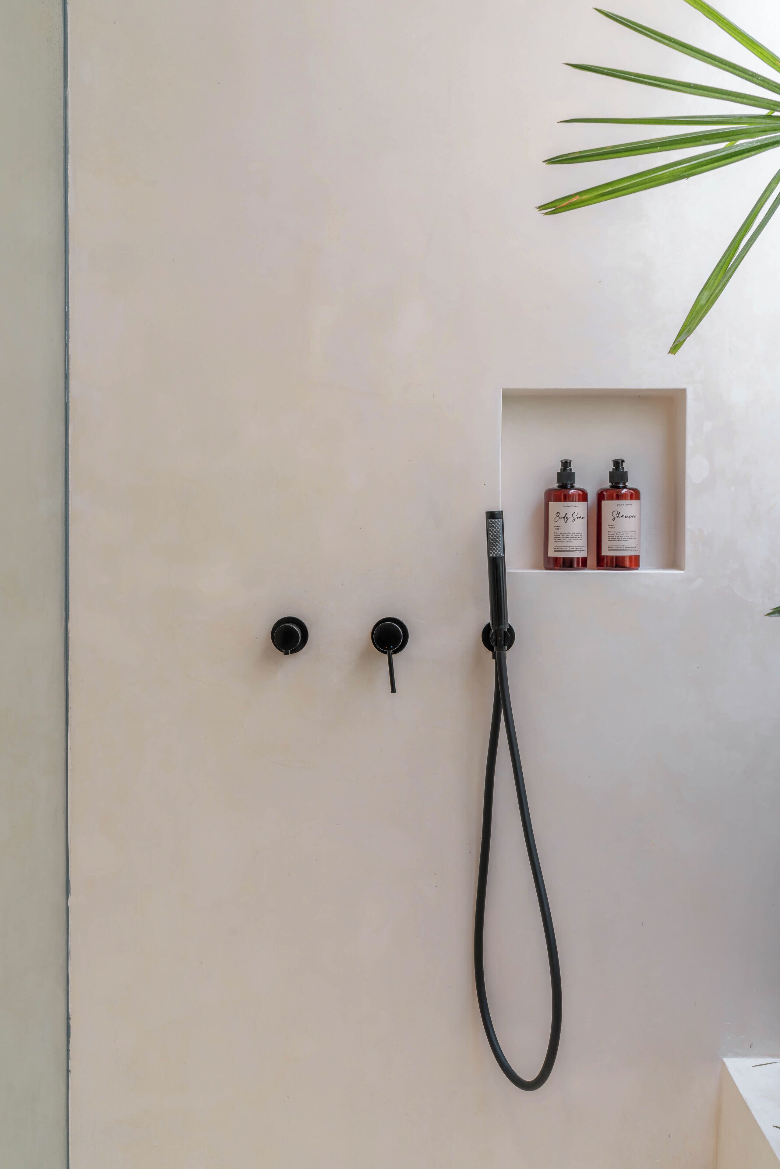 Une salle de bain avec une douche, deux robinets noirs et une étagère sur laquelle se trouvent deux bouteilles.