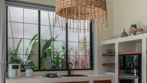 A modern kitchen with a large window, a dining table with chairs, and a hanging light fixture. - Casa Melosa - Charming and Intimate Villa Nestled in Umalas (Kerobokan)