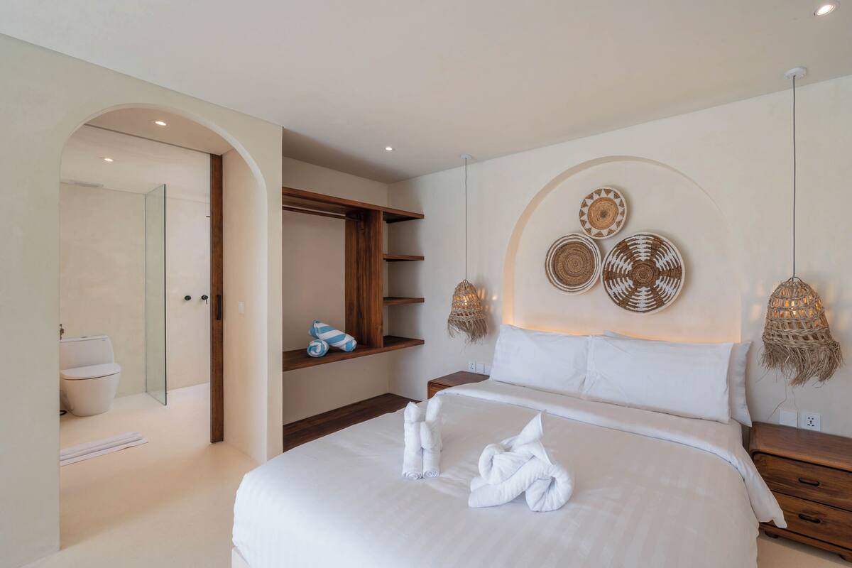 A modern bedroom with a large bed, a wooden nightstand, a built-in shelf, and a wall-mounted light fixture.