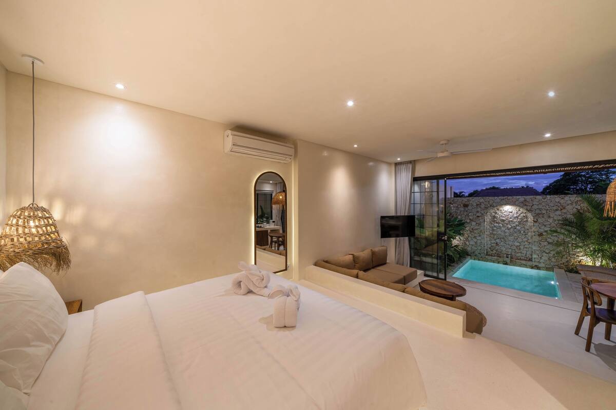 A modern bedroom with a large bed, a small sofa, a TV, and a view of a swimming pool.