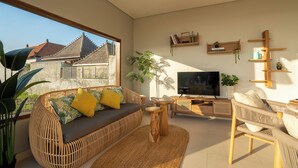 Een moderne woonkamer met een bank, stoelen, een televisie en een groot raam met uitzicht op een traditioneel huis.
