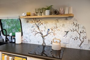 Eine Küche mit Mosaik-Spritzschutz, einem Holzbodenregal mit Gläsern und einem Wasserkocher auf der Arbeitsplatte.