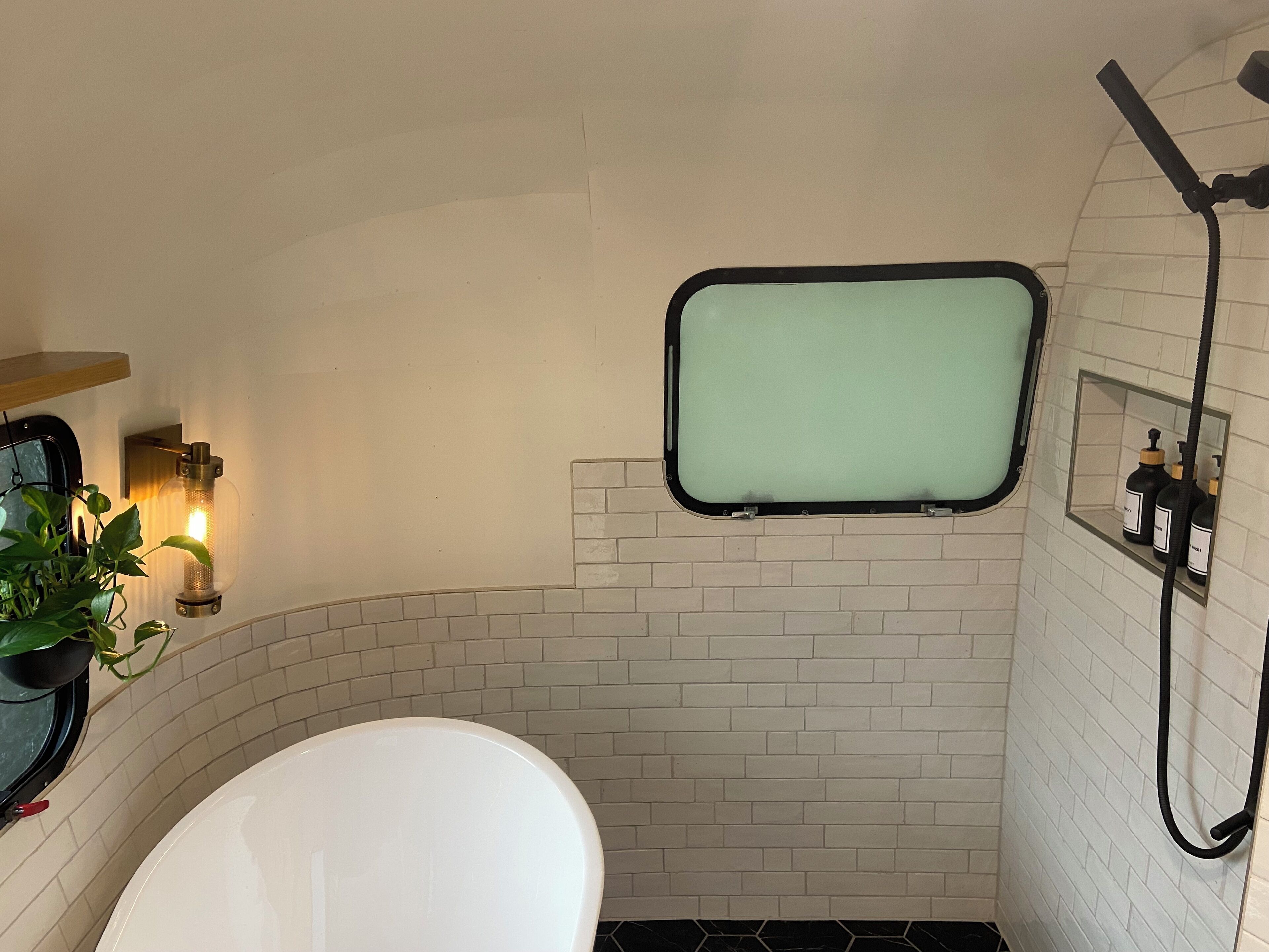 A bathroom with a white bathtub, a small window, and a shower area.