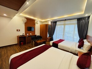 Quarto de hotel com duas camas, uma escrivaninha com cadeira, televisão e janela com cortinas.