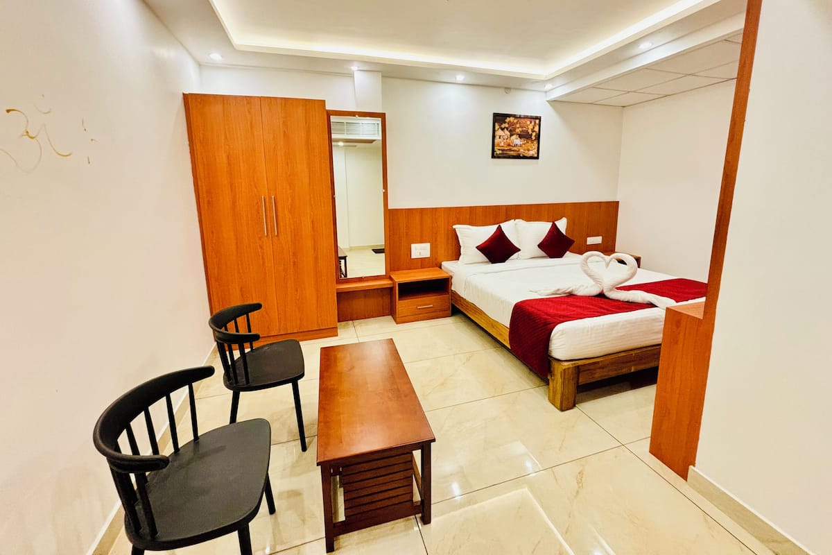 A hotel room with a bed, a wooden wardrobe, a desk, two chairs, and a mirror.