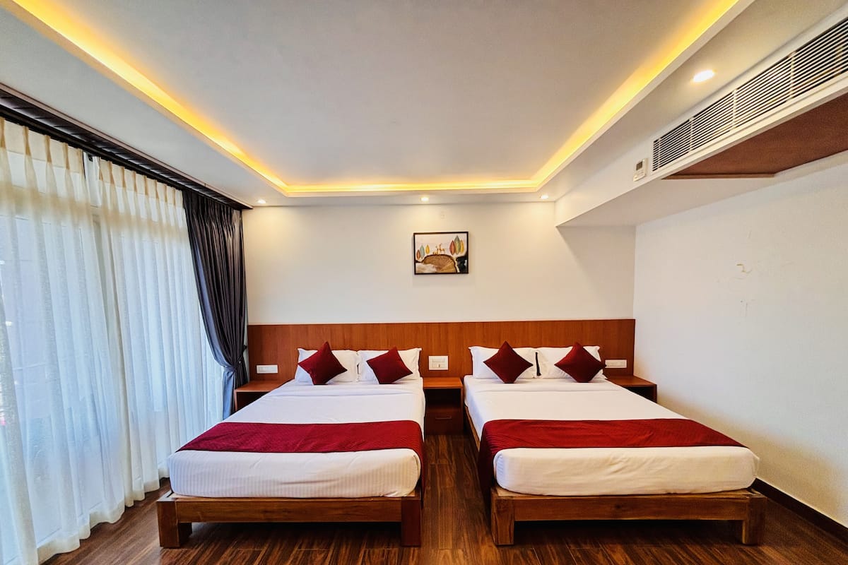 A hotel room with two beds, wooden flooring, a painting on the wall, and a window with curtains.