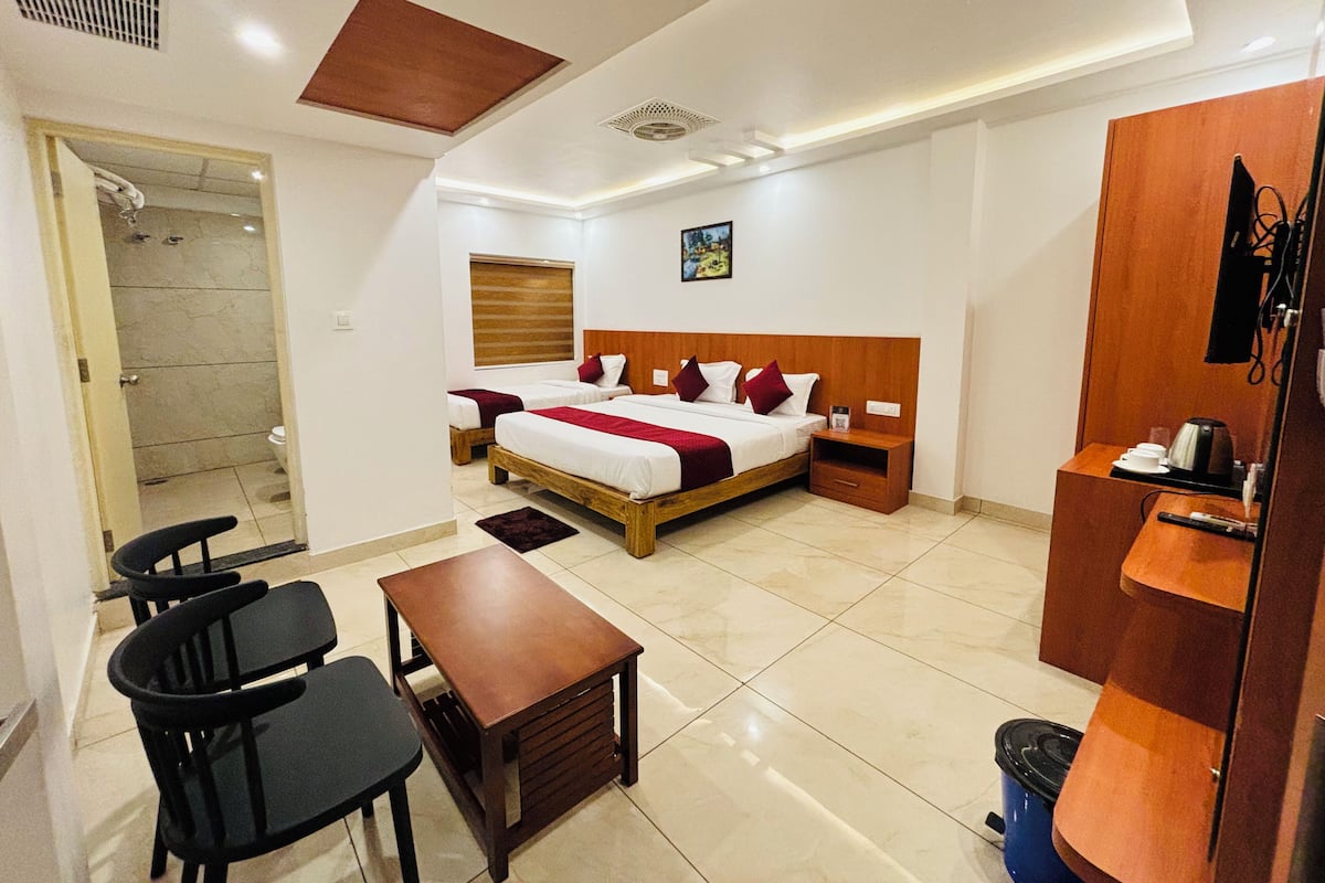 A hotel room with a bed, two bedside tables, a desk with chairs, a wardrobe, and a bathroom with a shower and toilet.