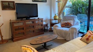 A living room with a television, wooden cabinet, sofa, and a view of greenery outside. - Family duplex overlooking the beach (Antibes)