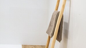 Una habitación con suelo de madera, paredes blancas con textura y un caballete de madera apoyado contra la pared con una toalla colgada.