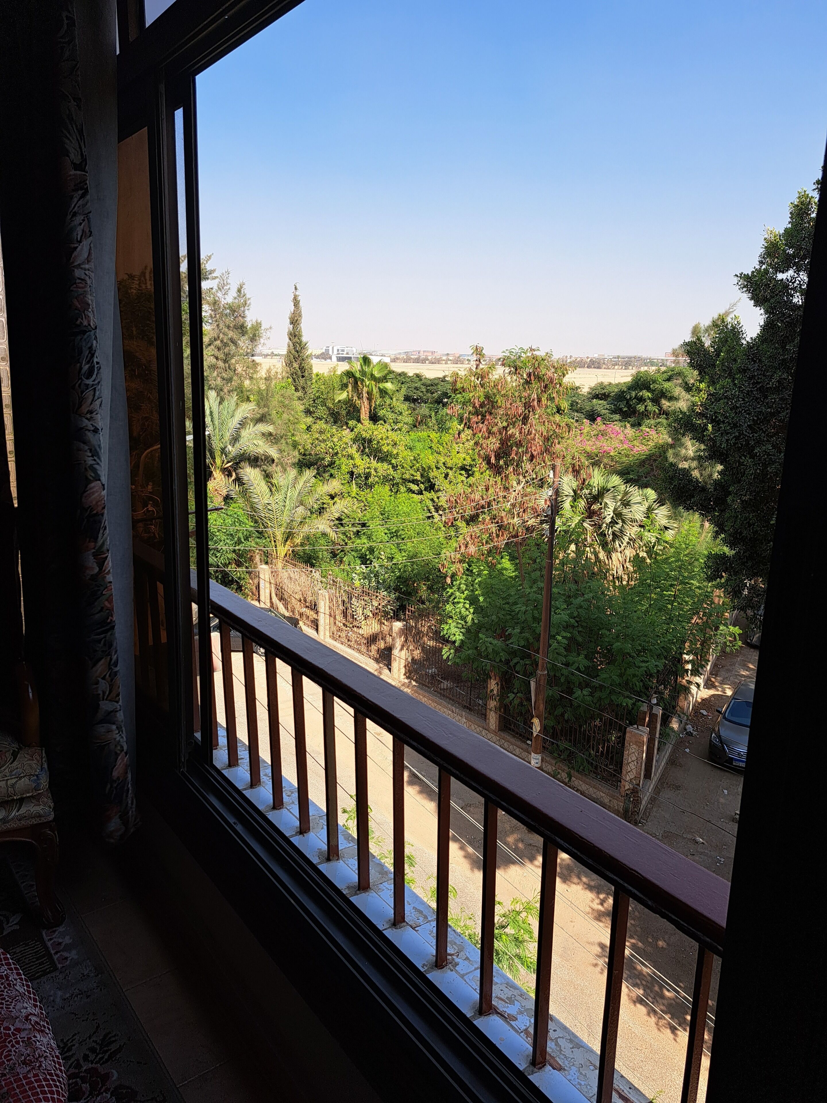 Un balcón con vistas a un jardín exuberante y un cielo azul despejado.