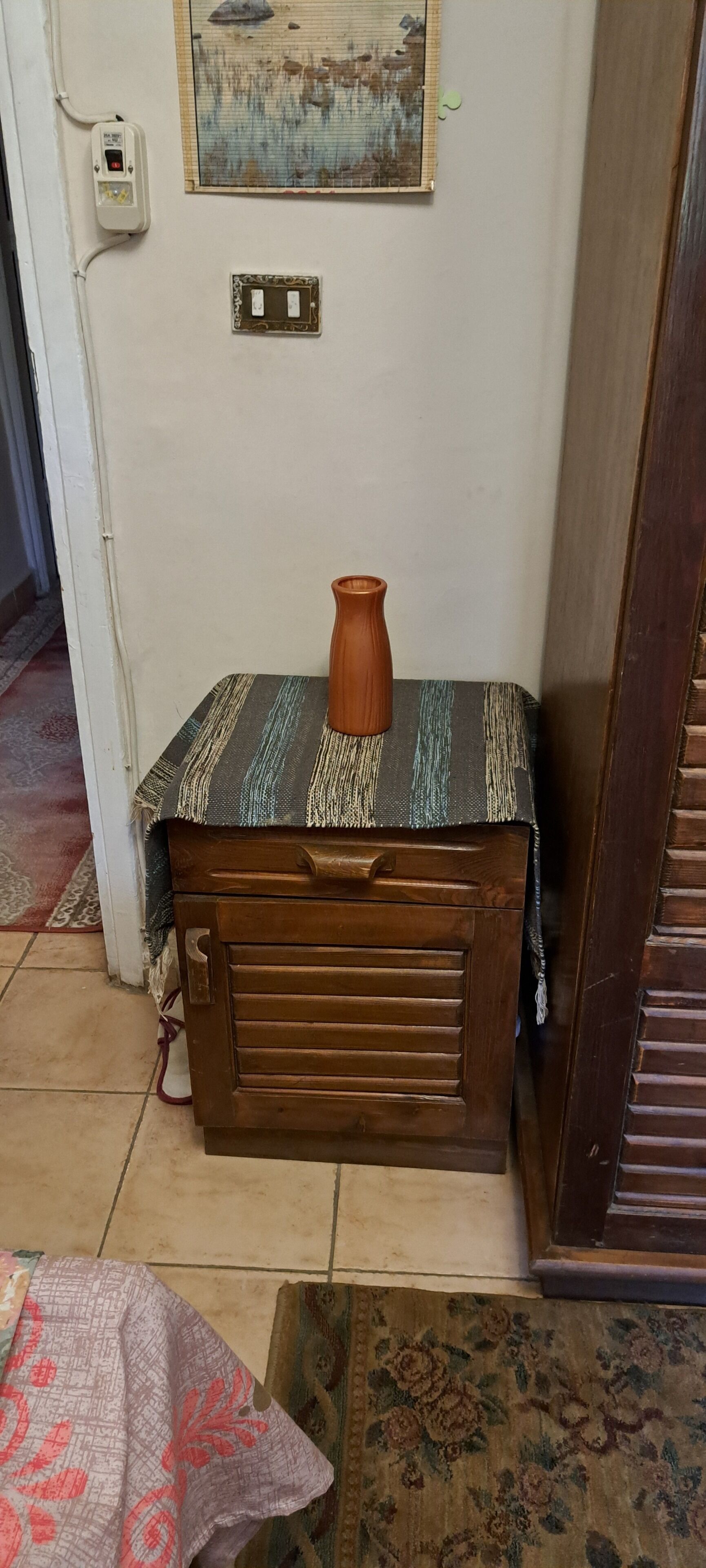 Ein Raumeck mit einem Holzschrank, einer Vase darauf, einer Steckdose und einem an der Wand montierten Lichtschalter.
