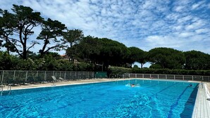 A clear blue swimming pool with a tiled deck, surrounded by trees and a metal fence.