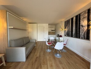 Un salon moderne comprenant un canapé, une table à manger avec des chaises, un coin cuisine et un grand tableau accroché au mur.