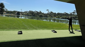 A view of a golf course with a pond, trees, and a clear sky.