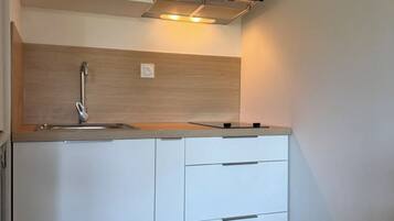A compact kitchen with a built-in oven, a sink, and a wooden backsplash.