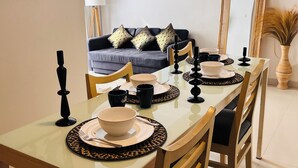 A dining area with a long table set for four, a sofa in the background, and a large mirror. - Casa Kuta View 2 BR (Kuta)