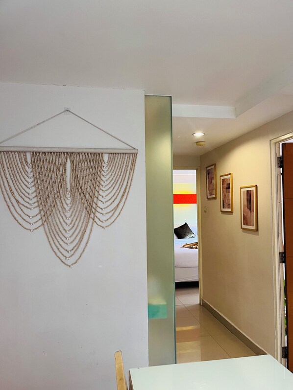 A hallway with a decorative wall art, a bed with pillows, and framed pictures on the wall. - Casa Kuta View 2 BR (Kuta)