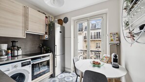 A compact kitchen with modern appliances, a dining area with a table and chairs, and a view of the city through a large window.