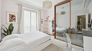 A bedroom with a bed, a desk, a chair, a bookshelf, and a large mirror.