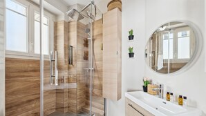 A modern bathroom with a glass-enclosed shower, wooden paneling, a white vanity with a mirror, and a small potted plant.