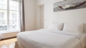 Une chambre avec un grand lit, une fenêtre avec des rideaux et un tableau au mur.