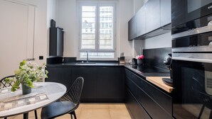 Une cuisine moderne avec des meubles de rangement noirs, une fenêtre, une table à manger avec des chaises et une petite plante en pot.