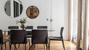 Un espace repas moderne avec un parquet en bois disposé en chevrons, une table ronde entourée de chaises, un luminaire suspendu et un miroir au mur.