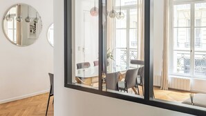 Un salon moderne avec une grande fenêtre, un miroir rond et une table en bois sur laquelle est posé un vase de fleurs.