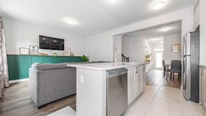 Eine moderne Küche mit integriertem Geschirrspüler, einem grauen Sofa und einem Essbereich mit Tisch und Stühlen.