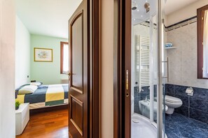 Un dormitorio con cama, mesita de noche y ventana. El suelo es de madera y las paredes son de color verde claro.