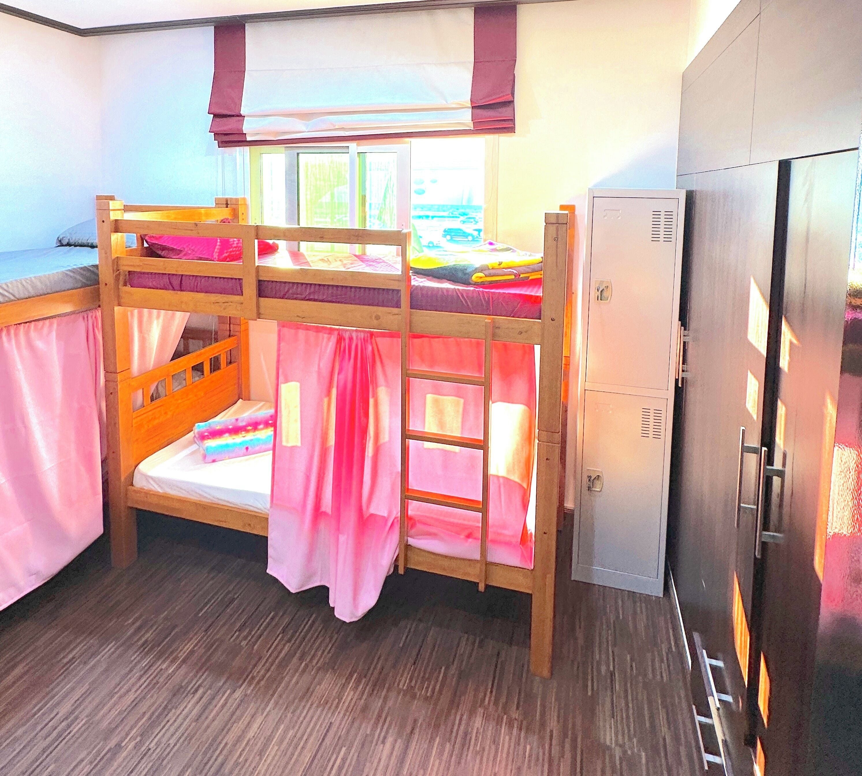 A bunk bed room with a window, a wardrobe, and a refrigerator.