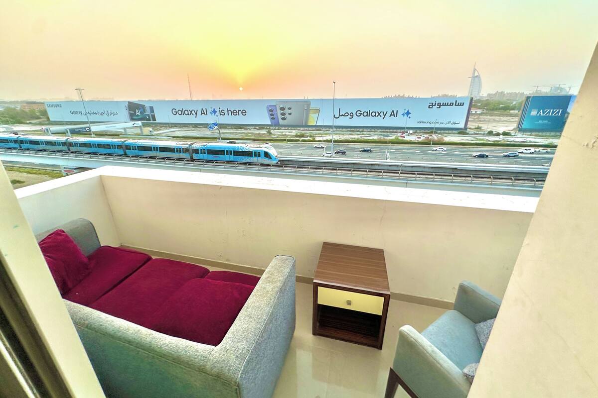 A balcony with a view of a train passing by, a Samsung Galaxy sign, and a small table.